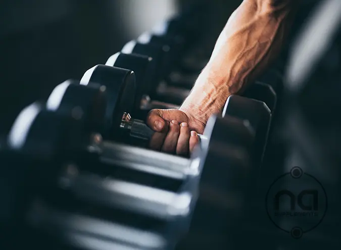 male clasping dumbbell in the gym